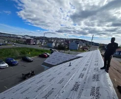 Crew member standing on a roof deck covered in underlayment under a blue sky